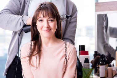 Erkek stilisti bir kadınla güzellik salonunda çalışıyor.