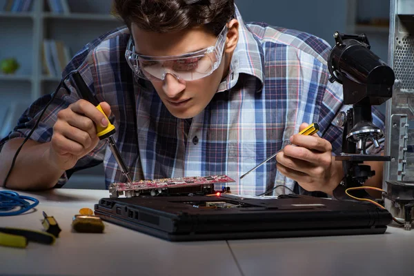 Young repair technician soldering electrical parts on motherboar