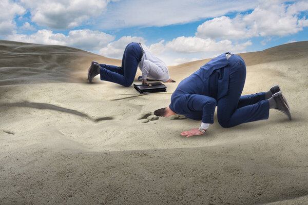 Бизнесмен прячет голову в песок, спасаясь от проблем.