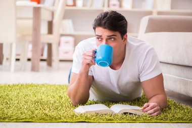 Adam evde yerde kitap okuyor.