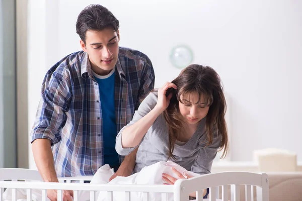 Young parents with their newborn baby near bed cot — Stock Photo, Image