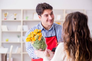 Çiçekçi yardımcısı kadın müşteriye çiçek satıyor.