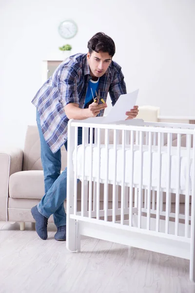 Jovem montando cama de bebê com manual de instruções — Fotografia de Stock