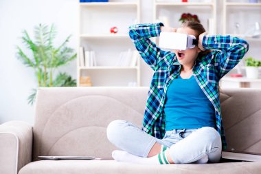 Kanepede oturan sanal gözlüklü kız öğrenci.