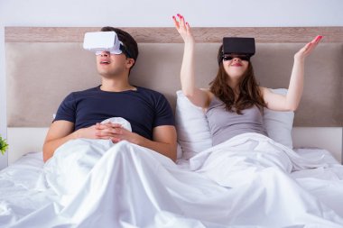 Yatakta sanal gerçeklik gözlüklü eş ve koca.