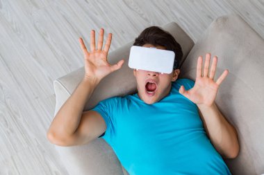 VR gözlüklü genç adam kanepede dinleniyor.