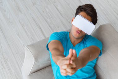 VR gözlüklü genç adam kanepede dinleniyor.