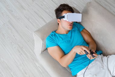 VR gözlüklü genç adam kanepede dinleniyor.