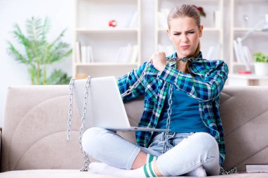 Dizüstü bilgisayarlı, kanepede oturan zincirlenmiş bir kız öğrenci.