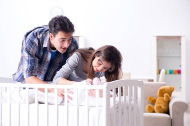 Yatağın yanında yeni doğmuş bebekleri olan genç ebeveynler.