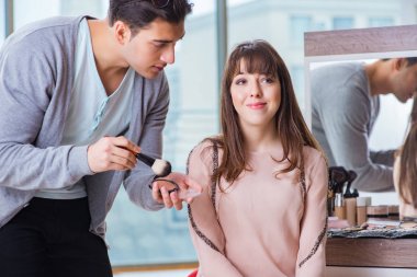 Güzellik salonunda güzel bir kadın için makyaj yapan adam.