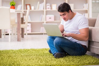 Evde, halı döşemesinde dizüstü bilgisayarda çalışan bir adam.
