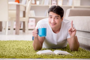 Adam evde yerde kitap okuyor.