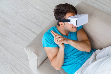 VR gözlüklü genç adam kanepede dinleniyor.