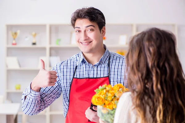 Çiçekçi yardımcısı kadın müşteriye çiçek satıyor.