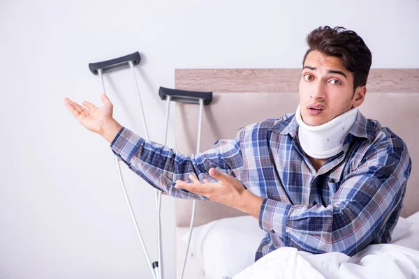 Injured man in bed at home with crutches — Stock Photo, Image
