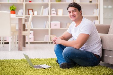 Evde, halı döşemesinde dizüstü bilgisayarda çalışan bir adam.