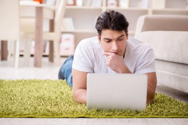 Evde, halı döşemesinde dizüstü bilgisayarda çalışan bir adam.