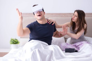 Yatakta sanal gerçeklik gözlüklü eş ve koca.