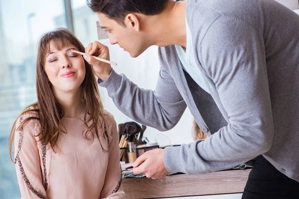 Güzellik salonunda güzel bir kadın için makyaj yapan adam.