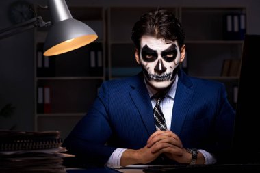 Korkunç maskeli bir iş adamı ofiste geç saatlere kadar çalışıyor.