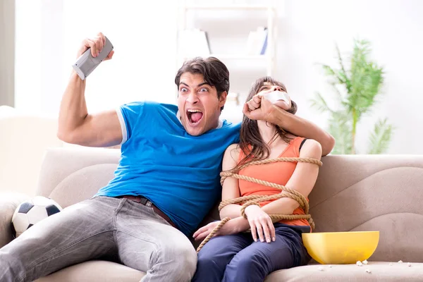 Man tying up his wife to watch sports football — Stock Photo, Image