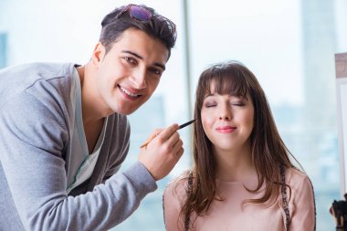 Güzellik salonunda güzel bir kadın için makyaj yapan adam.