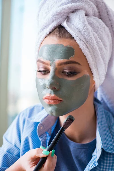 Woman applying clay mask with brush at home