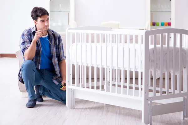 Young man assembling baby bed with instruction manual — Stock Photo, Image