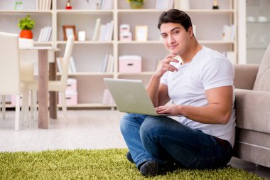 Evde, halı döşemesinde dizüstü bilgisayarda çalışan bir adam.