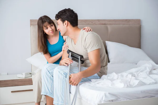 Young wife supporting husband on crutch after injury — Stock Photo, Image