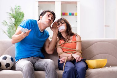 Adam spor maçı izlemek için karısını bağlıyor.