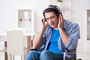 Tekerlekli sandalyede müzik dinleyen engelli adam.
