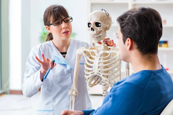 Doctor showing type of injury on skeleton to patient — Stock Photo, Image