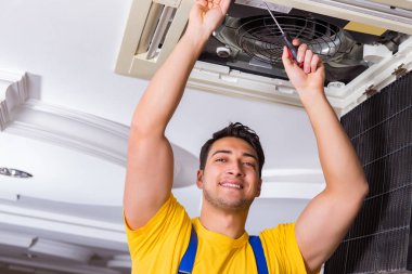 Tamirci tavan havalandırma ünitesini tamir ediyor.