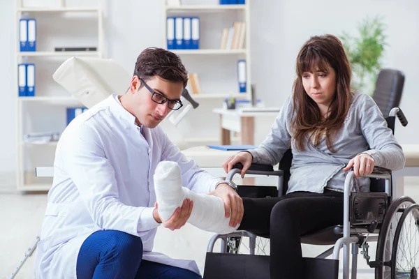 Erkek doktor tekerlekli sandalyedeki kadın hastayı muayene ediyor.