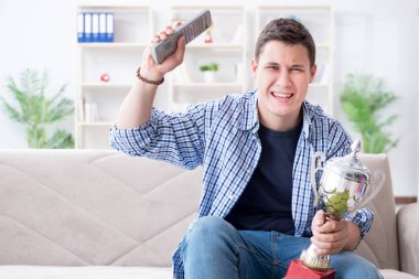 Evde futbol izleyen genç bir öğrenci.