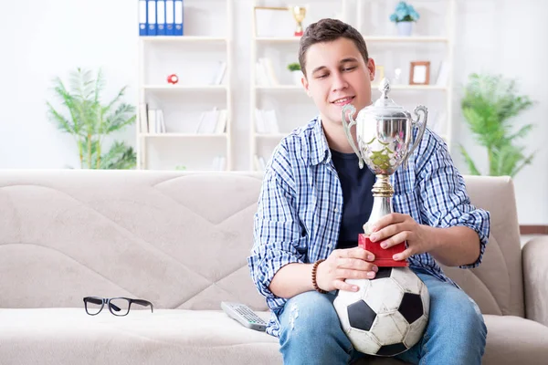 Evde futbol izleyen genç bir öğrenci.