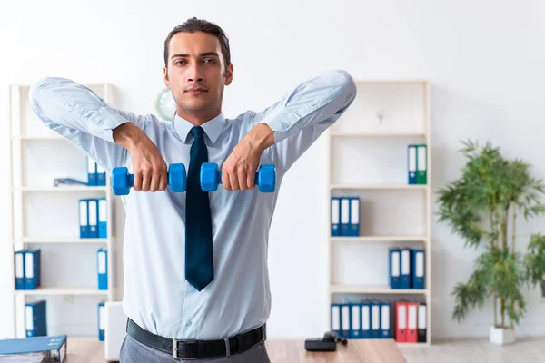 Joven empleado guapo haciendo ejercicios deportivos en el lugar de trabajo —  Fotos de Stock