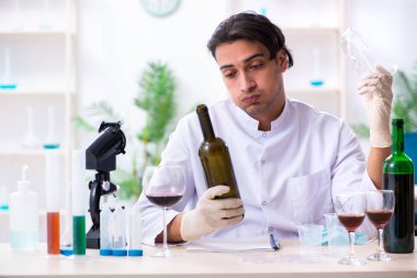 Erkek kimyager laboratuvarda şarap örneklerini inceliyor.