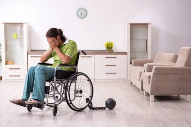 Evde acı çeken tekerlekli sandalyede yatan genç bir erkek.