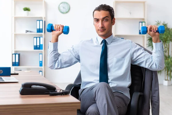 Joven empleado guapo haciendo ejercicios deportivos en el lugar de trabajo —  Fotos de Stock