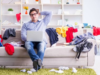 Genç adam dağınık bir odada çalışıyor.