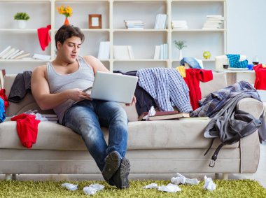 Genç adam dağınık bir odada çalışıyor.