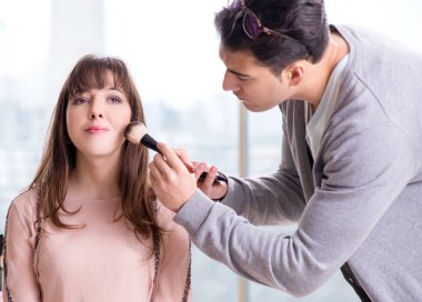 Güzellik salonunda güzel bir kadın için makyaj yapan adam.