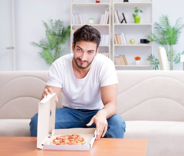 Pizza yiyen adam evde yemek yiyor, dinleniyor.