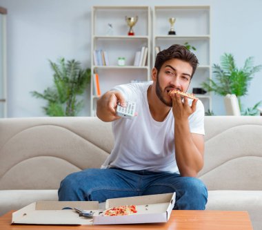 Pizza yiyen adam evde yemek yiyor, dinleniyor.