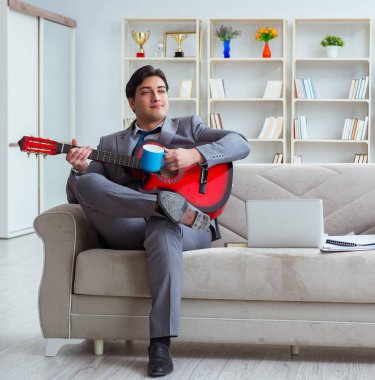 Evde gitar çalan bir iş adamı.