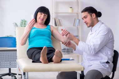 Genç erkek doktor yaşlı kadın hastayı muayene ediyor.