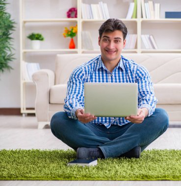 Genç yakışıklı adam evde yerde oturuyor.